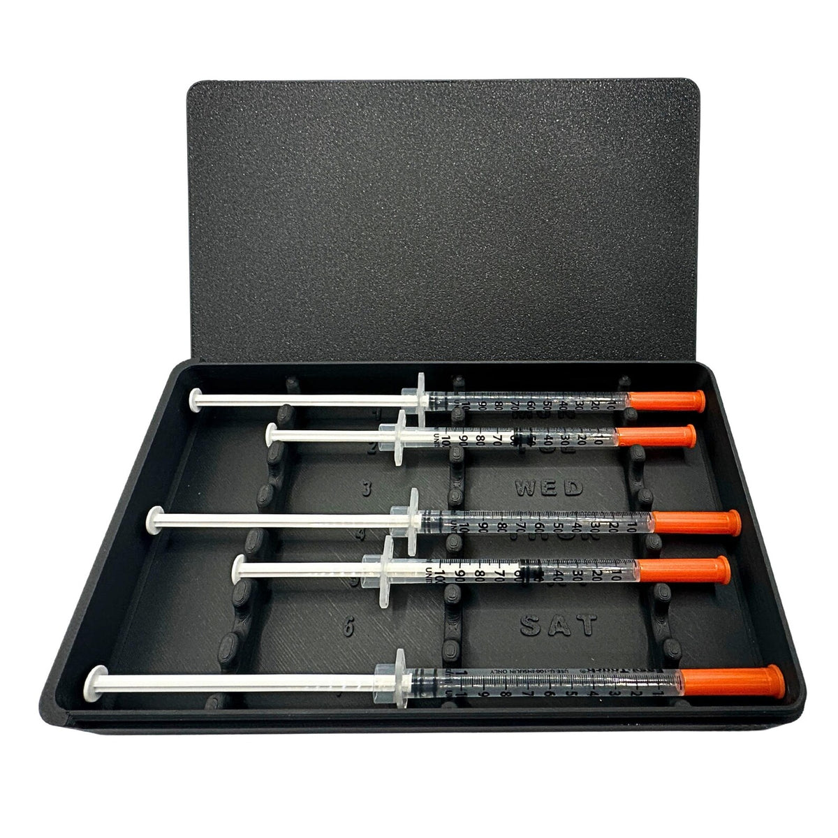 Prefilled syringe case with sliding lid open showing 5 of 7 slots loaded with 1ml insulin syringes. Day-of-week labels visible including Wednesday, Thursday, Saturday. Weekly syringe organizer for daily dosing routine tracking. Black syringe storage case for fridge, travel, or drawer organization.