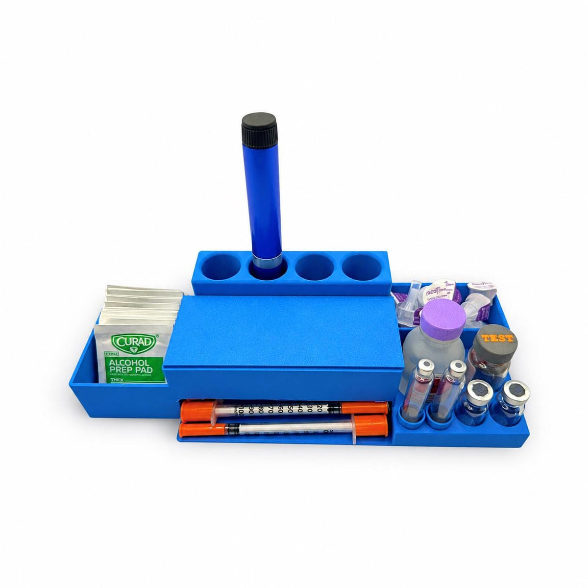 Blue desktop injection organizer on white with a syringe dispenser, four rear pen slots, vial and cartridge holders, alcohol prep pads and packaged pen needles.