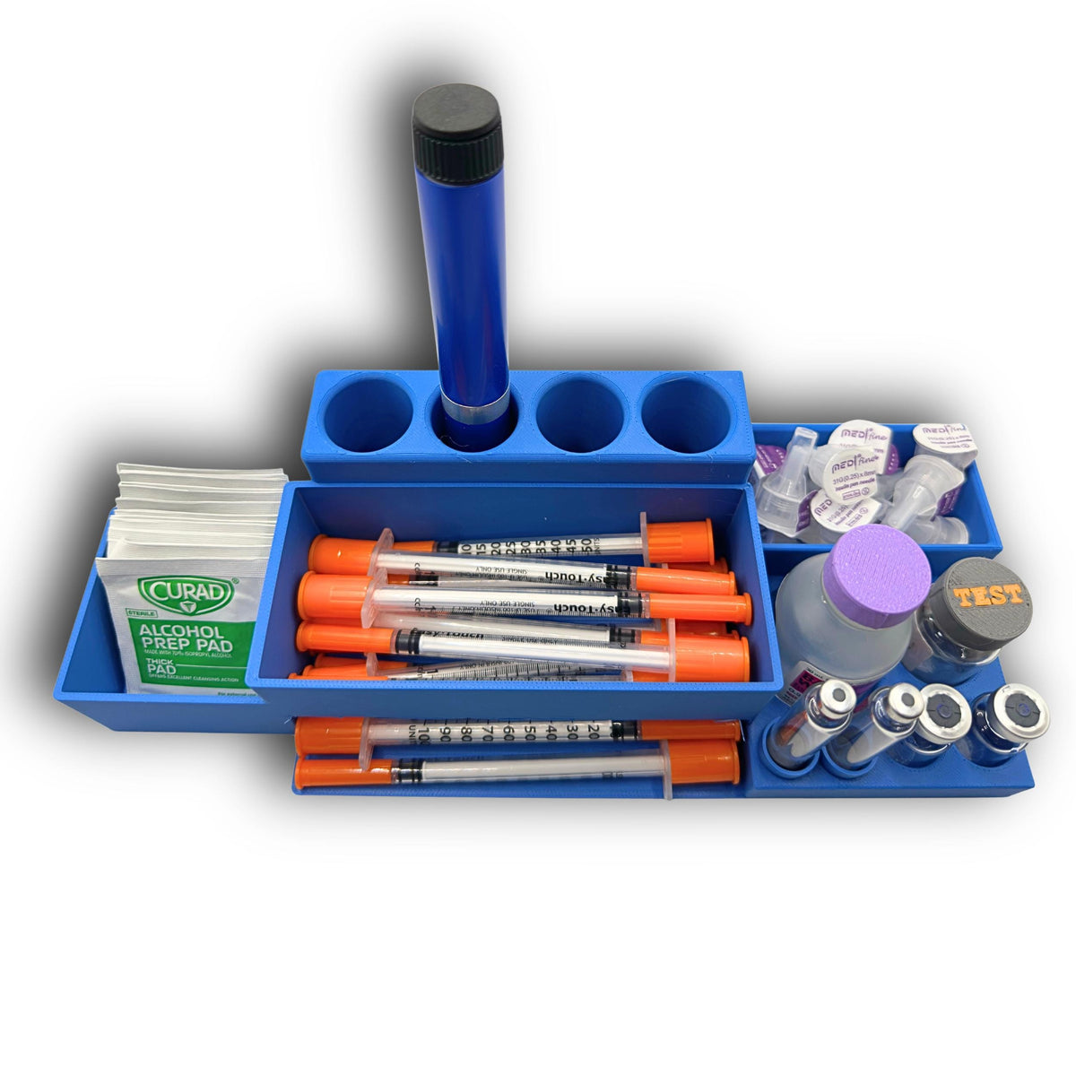 Desktop injection organizer with the dispenser lid removed, showing stored syringes beside alcohol wipes, an injection pen, cartridges and vials.